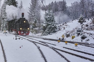 Dumanı tüten ve bacası karlı düğmelere yönelen buharlı bir lokomotif.