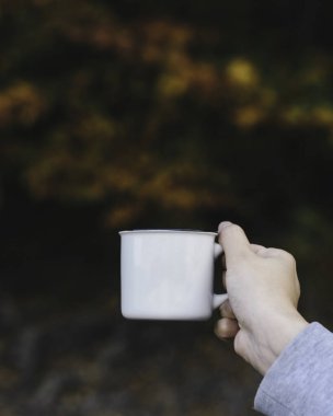 Sonbahar yapraklarında kahve fincanı tutan bir elin seçici odak noktası.