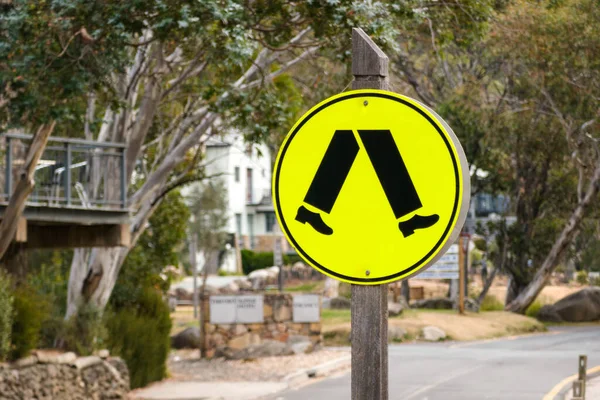 A closeup of a yellow street sign with feet