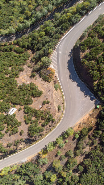 A vertical aerial shot of an asphalt road passing through a forested area
