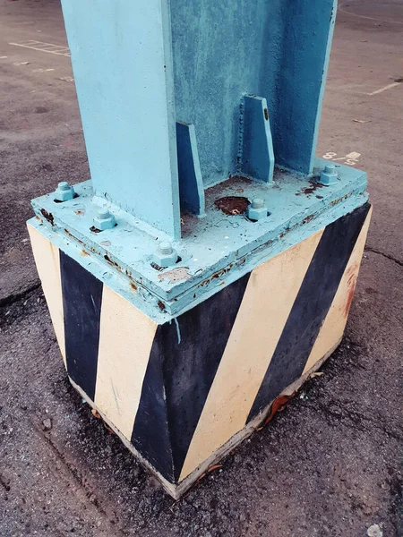 A closeup shot of blue metal pillar fastened to cement block with anchor bolts and nuts during daytime