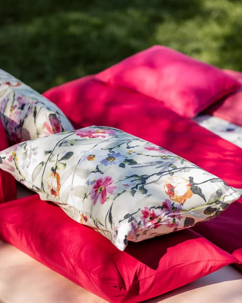 ピクニックのために草の上に花とピンクのベッドシートと枕の明るい垂直ショット — ストック写真