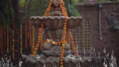 Turuncu kadife çiçekli çelenklerle süslenmiş taştan bir çeşmeden fışkıran suyun yavaşlaması.