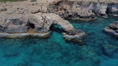 Güneşli bir günde, turkuaz bir denize karşı kayalık bir uçurum manzarası.