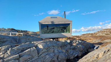 Norveç 'in güneyinde geniş panoramik pencereli minyatür bir kulübe var ve kayaları delen atların üzerinde duruyor..