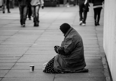 Yerde oturup para isteyen yaşlı bir kadının gri tonlu bir fotoğrafı. Yoksulluk kavramı.