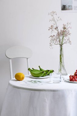 Dikey bir sandalye ve meyve dolu bir masa ve arka planda beyaz bir duvar vazosu.