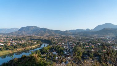 Bir kasabada bir nehir ve mavi gökyüzünün altında dağlar olan güzel bir manzara.