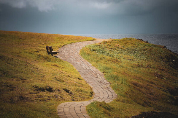 A stone walking path with two sides surrounded by lawn in the background of a seascape.