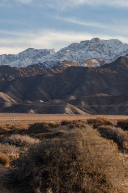 Terkedilmiş tepelerin dikey görüntüsü. Karlı dağların arka planında, bulutsuz gökyüzünün altında.