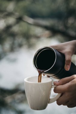 Bardağa kahve dökülen termosun seçici odak noktası.
