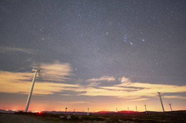 Portekiz 'in Arouca şehrindeki bulutlu yıldızlı gökyüzünün altındaki bir tarlada dev rüzgar türbinlerinin panoramiği.