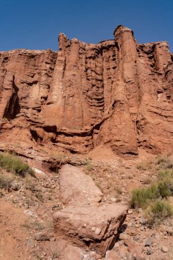 Bulutsuz bir gökyüzünün altında kayalık uçurumlar olan kırmızı taştan bir çölün dikey görüntüsü.