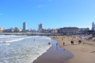 Güneşli bir günde Arjantin 'in mavi gökyüzüne karşı arka planda Mar del Plata şehri manzaralı Playa Bristol plajında güzel bir çekim yapan tatilciler.