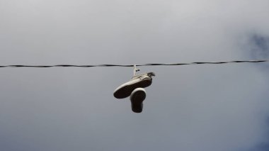 Bulutlu bir gökyüzüne karşı ipte sallanan eski bir çift ayakkabının alçak açılı çekimi.