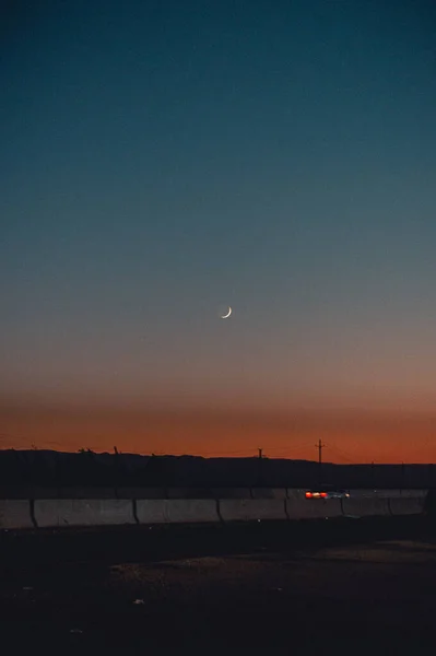 夕阳西下的新月形月亮的一个垂直镜头 一辆汽车从旁边经过 — 图库照片