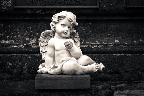 A grayscale shot of a little angel sculpture outdoors in the park