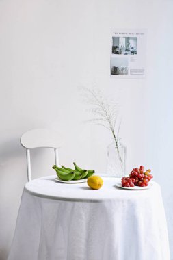 Dikey bir sandalye ve meyve dolu bir masa ve arka planda beyaz bir duvar vazosu.