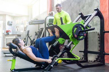 Kişisel antrenör, genç beyaz bir kadına koçluk yapıyor. Spor salonunda bacak egzersizi yapıyor. Spor konsepti.