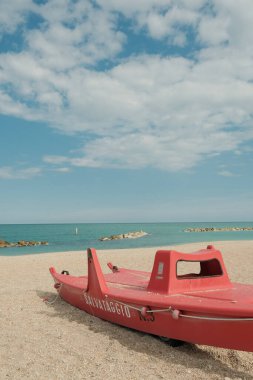 Güneşli bir sabahta kumlu bir sahilde kırmızı bir tekne.