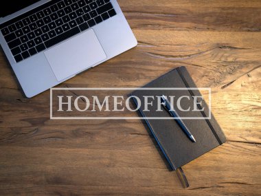 Açılmış bir dizüstü bilgisayarın ve İçişleri Bakanlığı 'ndan bir metnin olduğu ahşap bir masanın üzerinde bir defter. Evden çalışma kavramı.