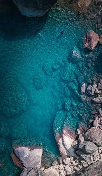 Kıyıdaki kayaların yakınındaki mavi deniz suyunun dikey görüntüsü.