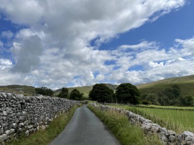 Yeşil tepeler ve bulutlu mavi gökyüzü olan taş bir duvar arasındaki güzel bir manzara.