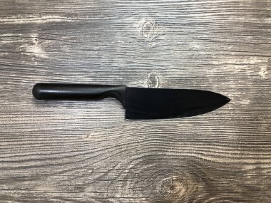 Masanın üzerinde duran siyah bıçak, ahşap bir dokuya sahip. Ahşap arka plandaki siyah bıçağın görüntüsünü kapat..