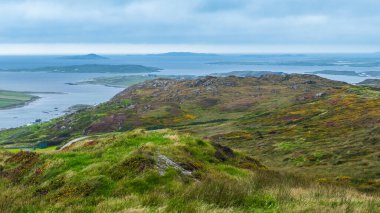 İrlanda 'da bulutlu bir günde, arkasında dağlar ve Atlantik Okyanusu olan güzel bir manzara.