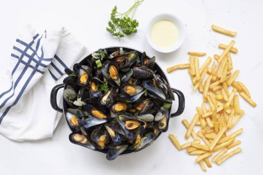 Beyaz mermer bir masada patates kızartması ve sos ile Belçika midyelerinin üst görüntüsü.