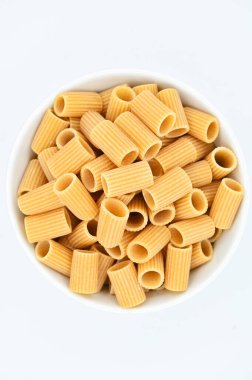 Beyaz arka planda beyaz bir kasede çiğ rigatoni makarna manzarası.