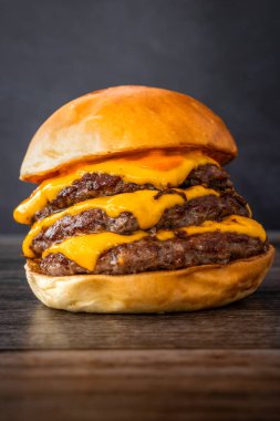 Lezzetli bir burgerin dikey görüntüsü, ahşap bir masada üçlü köfte.