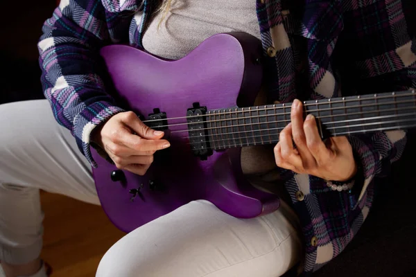 A person playing on a purple electronic guitar.