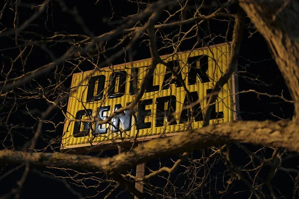 A closeup of the \'\'Dollar General\'\' sign with leafless tree branches in the foreground