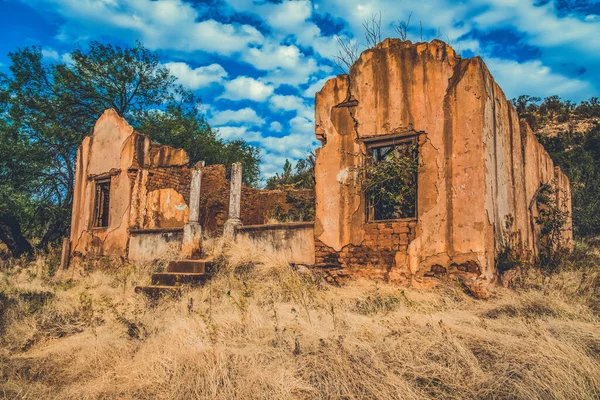 Terk edilmiş bir taş binanın manzarası mavi bulutlu gökyüzünün altında kurumuş bir tarlada harabe.