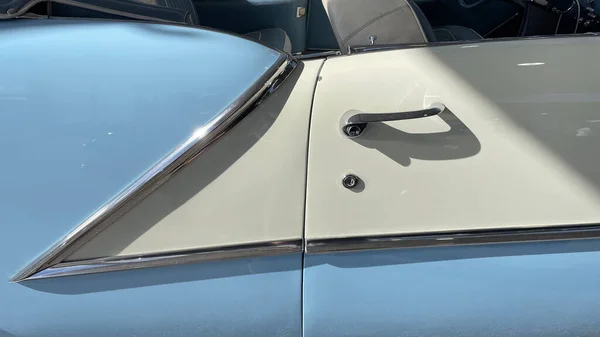 A door of a vintage blue and white car under the sunlight