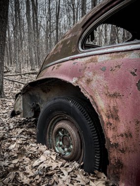 Ormanda terk edilmiş eski bir arabanın dikey görüntüsü.
