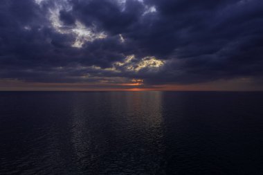 Gün batımında arka planda bulutlu gökyüzü olan sakin bir okyanus manzarası