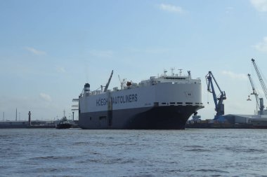 Güzel bir HOEGH Oto Gemisi bulutlu gökyüzünün altında vinçlerle limandan çıkıyor.