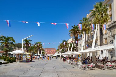 Bir grup insan güneşli bir günde Hırvatistan 'ın Split kentinde palmiye ağaçlarıyla çevrili güzel bir açık hava kafede eğleniyor.