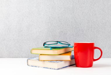 Yanında kitapların olduğu bir gözlüğün yakın plan fotoğrafı ve gri arkaplanda kırmızı bir kupa ve kopyalama alanı.