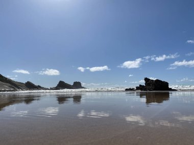 Okyanus dalgalarının güzel bir manzarası kayalara çarpıyor ve güneşli bir günde kumsala yuvarlanıyor.