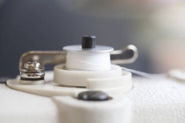 Bulanık arkaplanı olan bir dikiş makinesinin beyaz iplik rulosunun yakın plan çekimi.