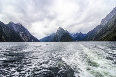 Büyük dağların arkasında su dalgaları olan bir deniz manzarası.