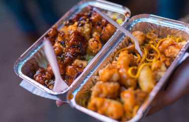 Elinde makarna ve soslu fast food tabağı olan gri bir kap tutan birinin yakın çekimi.