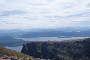 İskoçya 'da bulutlu bir günde tepelerle çevrili bir gölün arka planında güzel bir uçurum görüntüsü..