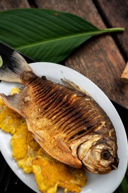 Tabakta pişmiş balık ve kızarmış muz resmi.