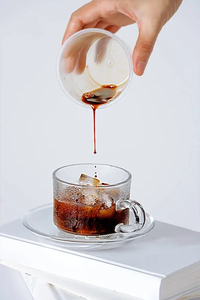 白い背景に氷のキューブとカップにコーヒーを徐々に追加する手の垂直ショット — ストック写真