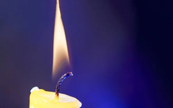 A closeup of the candlelight against the dark blue background.