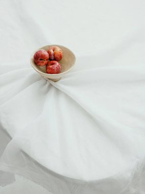 Beyaz kumaş kapaklı bir masada beyaz bir kasede elmaların dikey estetik görüntüsü.